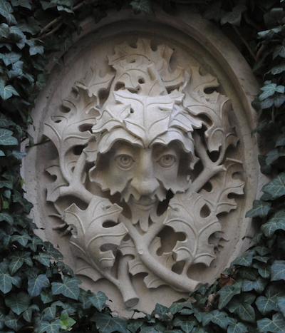Stone carving showing a bearded man's face emerging from a canopy of leaves.
