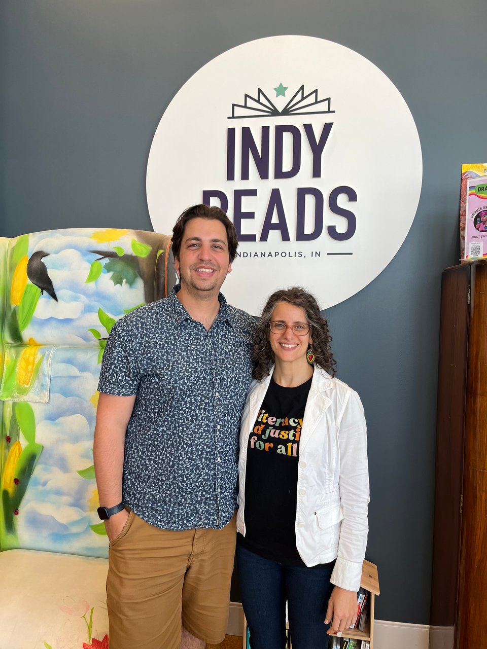 A photo of Michael Zarick and Ruba Marshood in front of the Indy Reads logo and a giant painted reading chair.