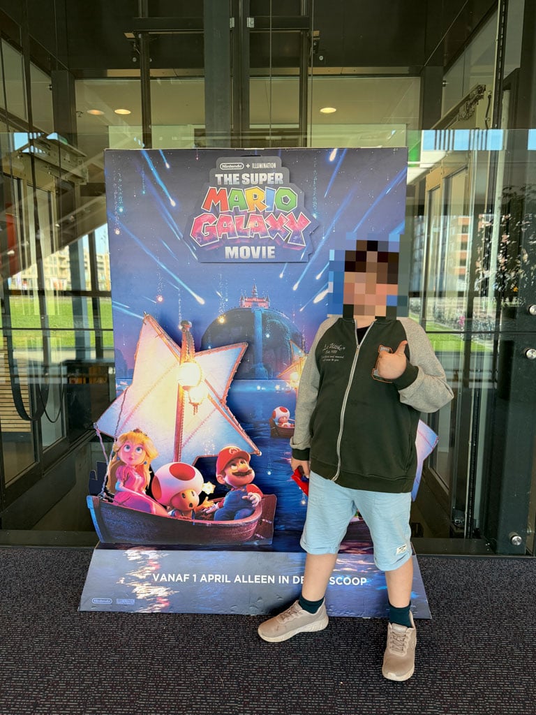 A boy stands in front of the 3-D poster for "The Super Mario Galaxy Movie" and has his thumb raised. His face is blurred.