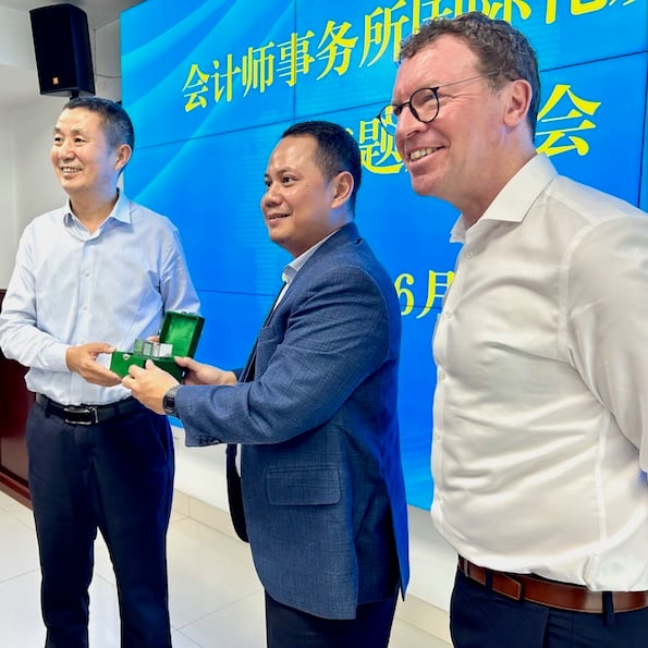 Three men standing in front of brightly coloured screens with Chinese writing. The man in the middle, Mikail Jaman, is giving an award. The man on the right is Andrew Menzies.