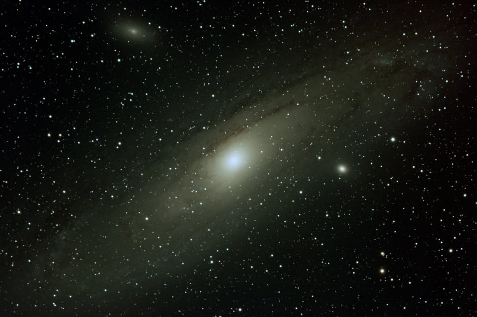 a very luminous galaxy against a dark background with lots and lots of stars plus two fuzzy, smaller galaxies surrounding it