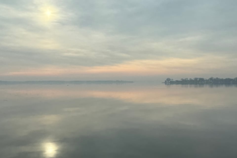 photo of water and sky on a hazy day with the cloud-obscured sun reflected below in the water
