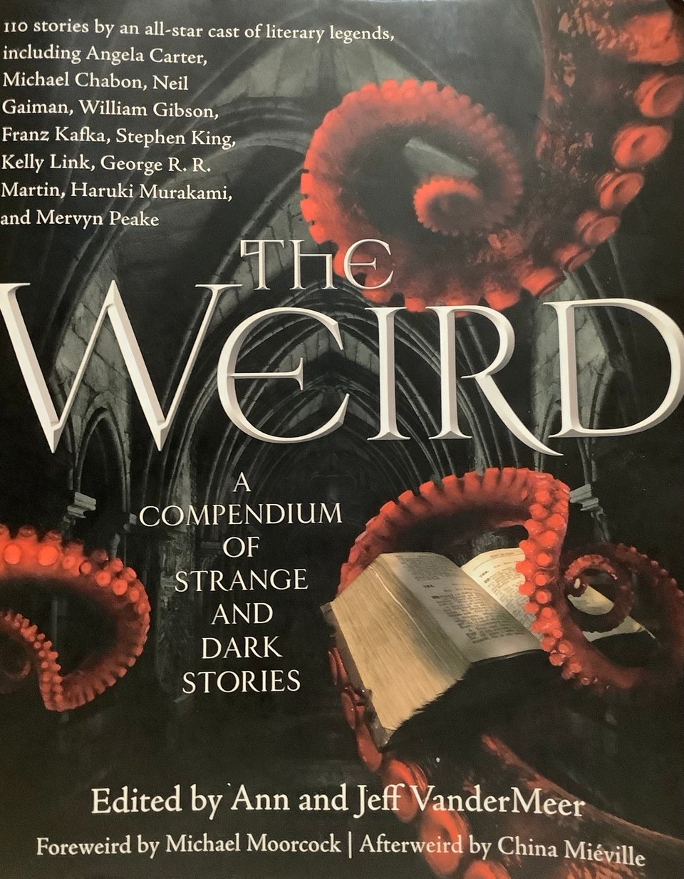 The cover of The Weird: A Compendium of Strange and Dark Stories edited by Ann and Jeff VanderMeer, Foreword by Michael Moorcock and Afterweird by China Miéville. Red octopus tentacles in a gothic crypt reach hold up a big, dense hardcover book