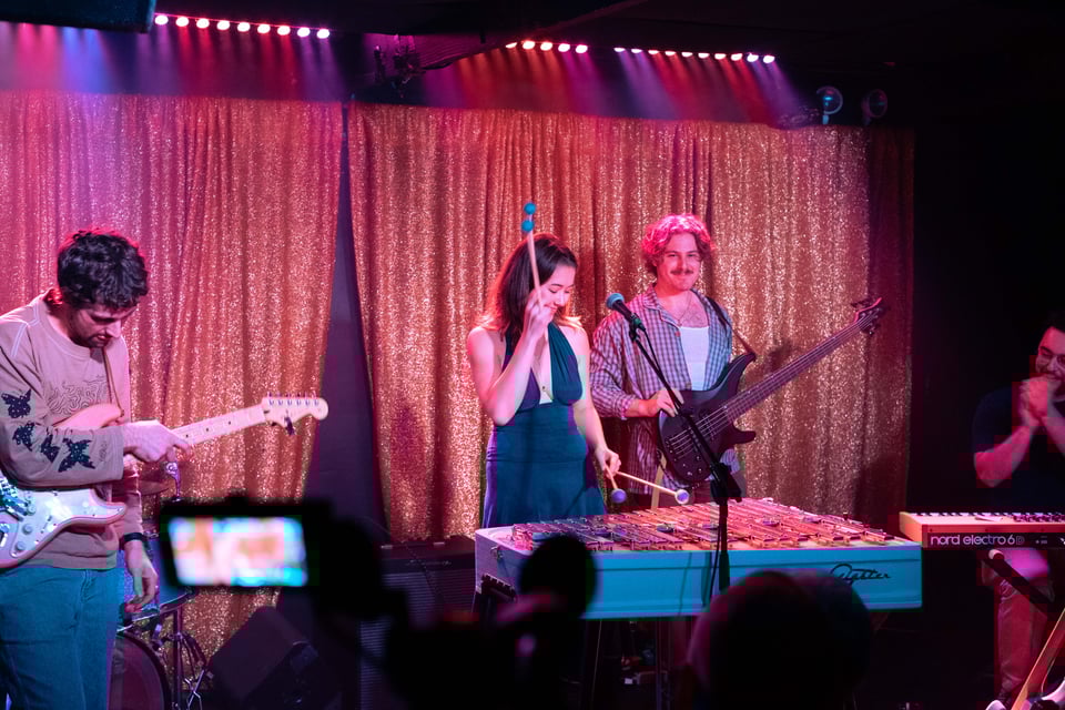 Sachi smiles on stage at C'mon Everybody, while the band and audience clap and grin