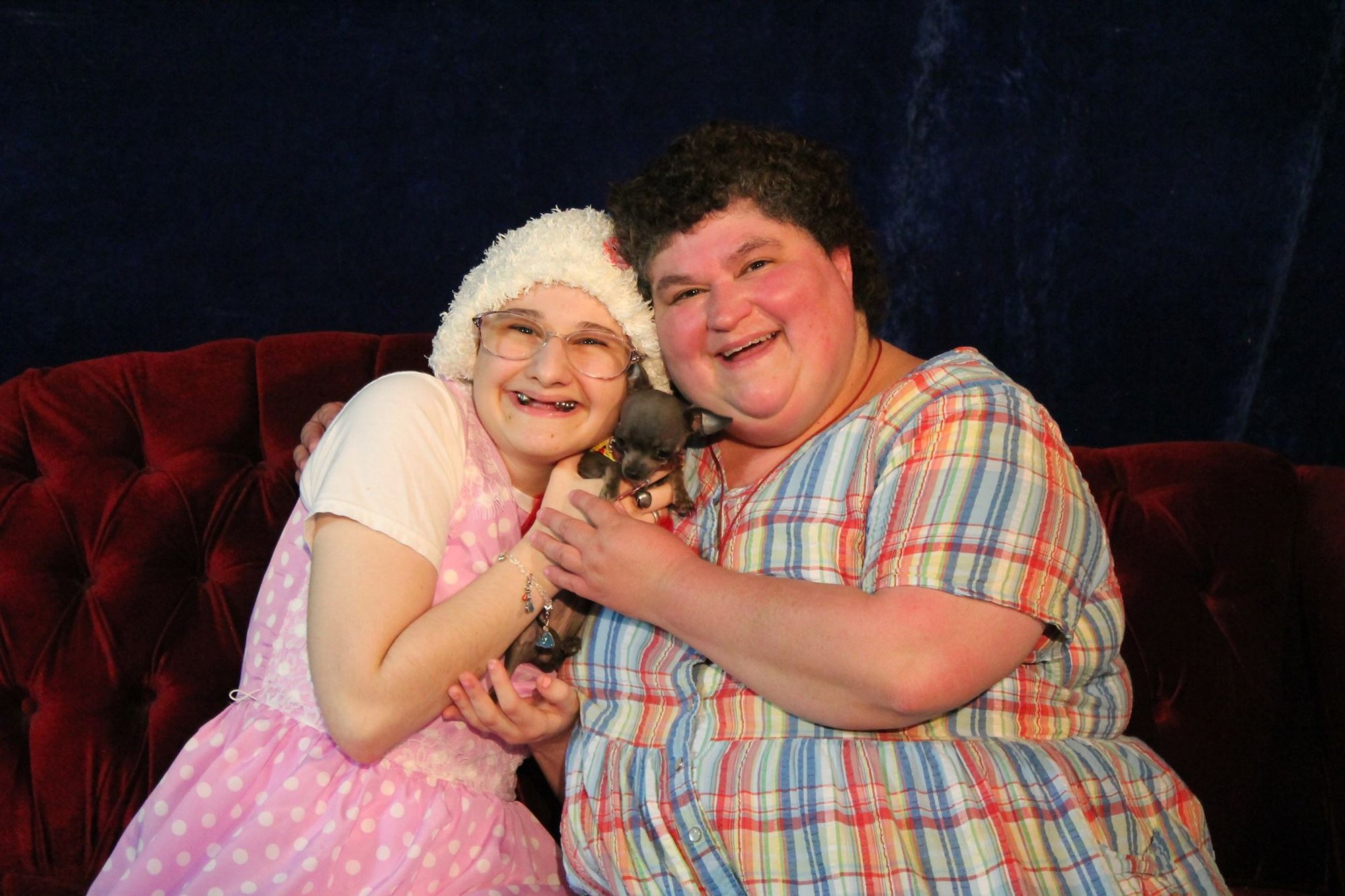 Gypsy Rose Blanchard and her mother Dee Dee pose together on a red couch, holding a small chihuahua puppy.