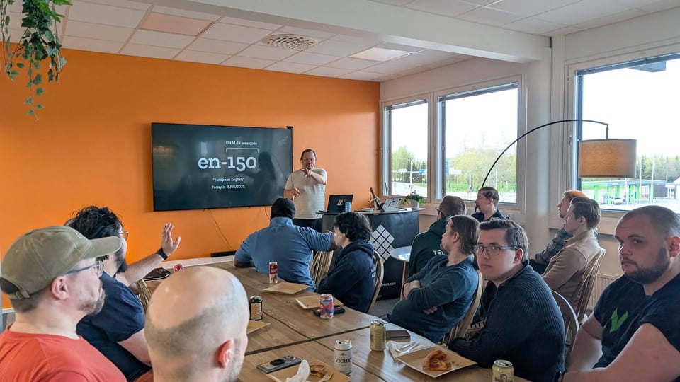 Eemeli speaking at the end of a room in front of a bright orange screen. In the room, there's a crowd listening.