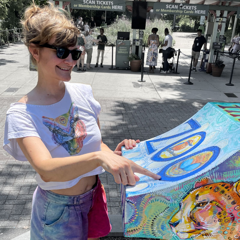 photo of a white person wearing sunglasses and pointing at a piece of public art