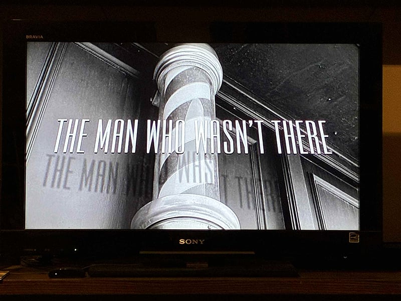 A photo of my television, which in this instant displays the title of the movie The Man Who Wasn't There in front of a black and white shot of a barber's pole.