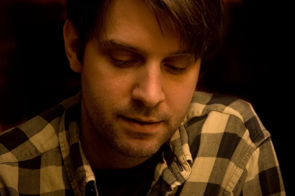 A close-up portrait of a man in a button-down checked shirt.