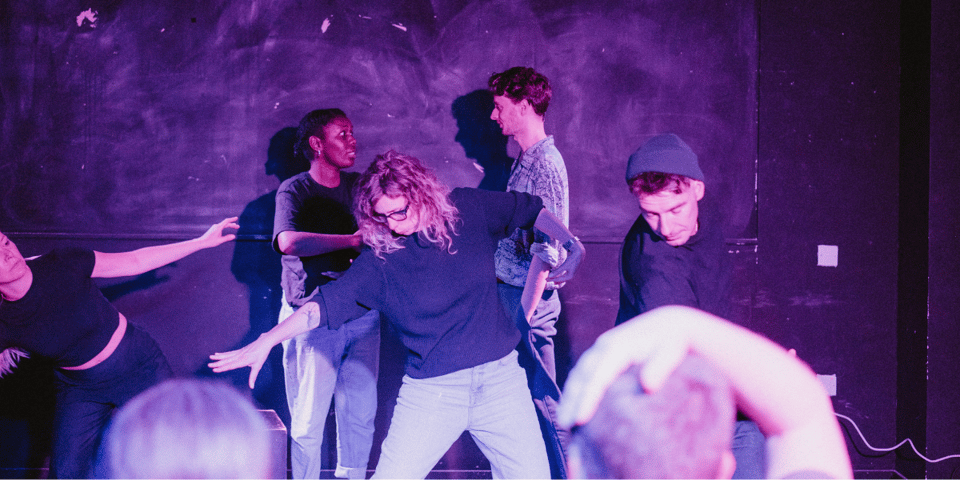 Improvisers moving around a purple stage.