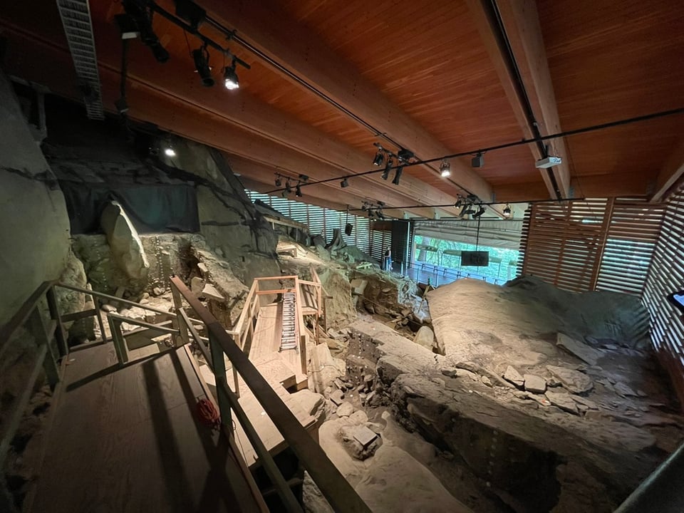 Huge slabs of rock with a wooden roof built overhead and wooden walkways built across the space. Lots of tiny archaeological labels are attached to the rock here and there.