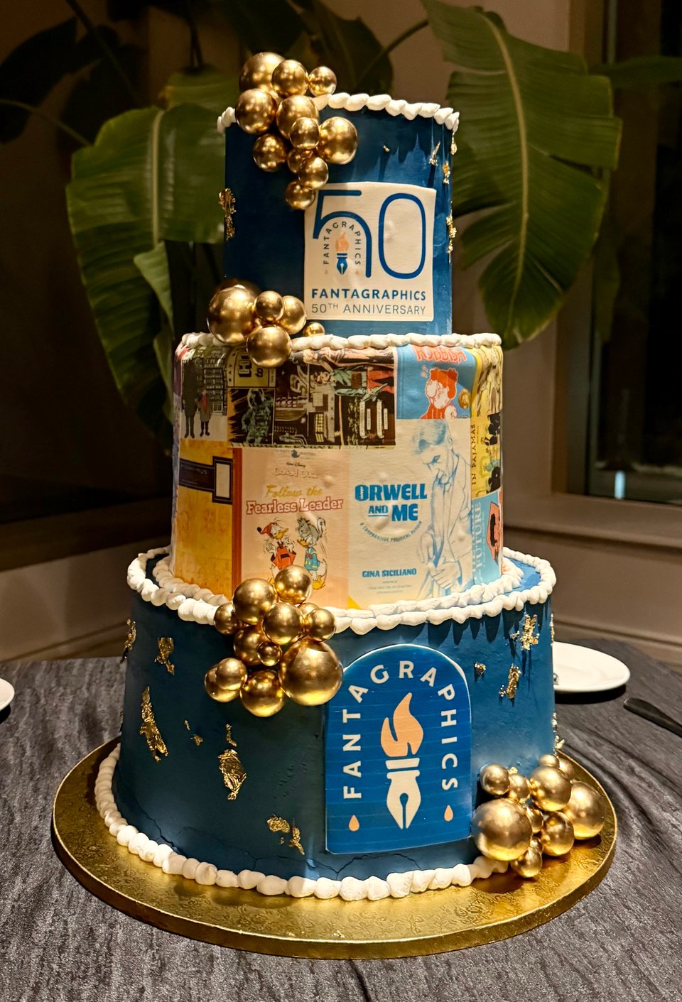 photo of a three-tier cake, celebrating Fantagraphics' 50th anniversary, covered with sheet-decor of various comic covers.
