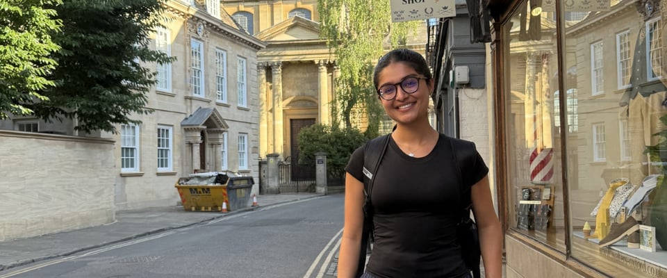 Photo shows Madison student Jasnoor Kaur during her travels abroad. She is posing outdoors and smiling, wearing glasses, a backpack and a black T-shirt.
