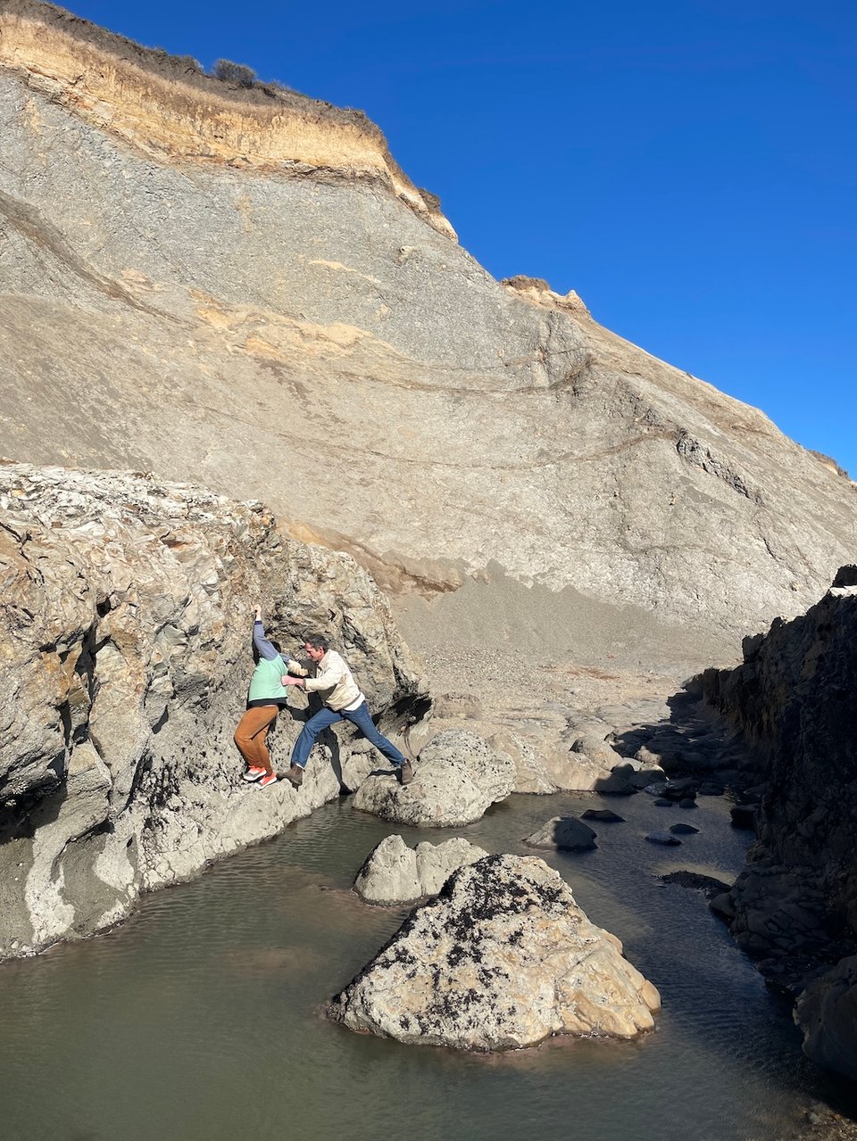 A man grabs the young boy from the back to steady him and get him back to safety from the rockface over the tide pool..