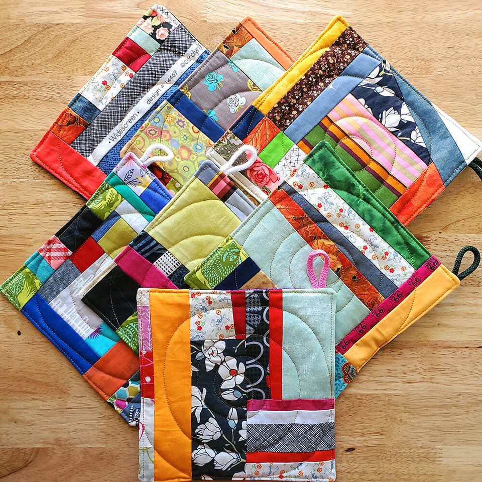 Top-down photo of Sarah's multicolored quilted potholders, arranged on a wooden table.