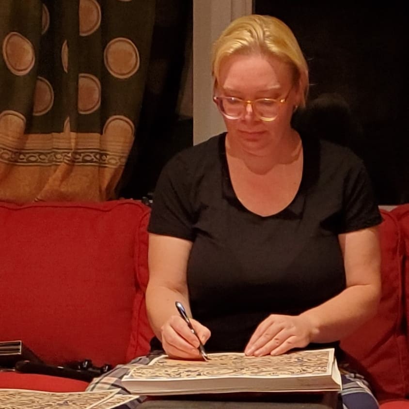 Kate is sitting on her couch in the evening, signing a stack of decorated pages.