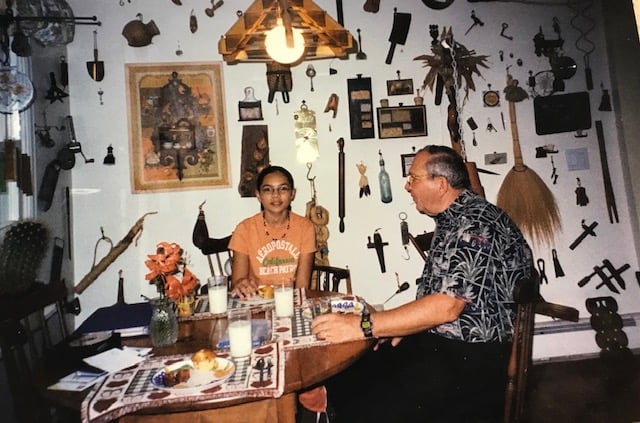 A photo of the author as a preteen, with her grandfather, in a kitchen. Behind her, a backdrop of a gallery wall with random tools and decorations nailed to the wall.