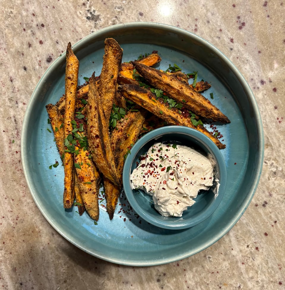 Thick wedges of sweet potato arranged on a blue plate flecked with parsley alongside a tahini dip.