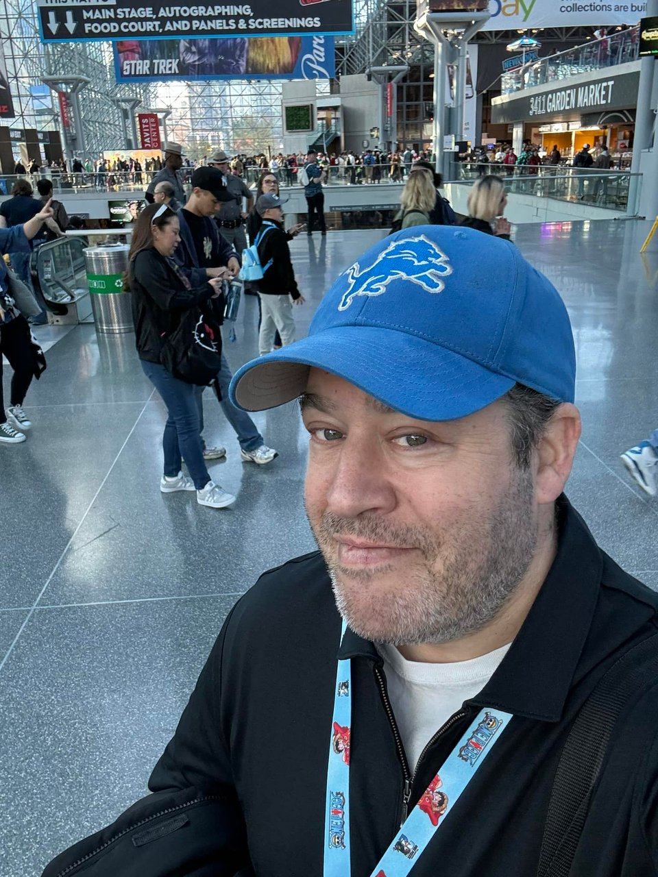 a photo of Neil Kleid in a black and white shirt and a blue and white Detroit Lions ball cap standing in the lobby of the Jacob Javits Convention Center in New York City, attending New York Comic-Con