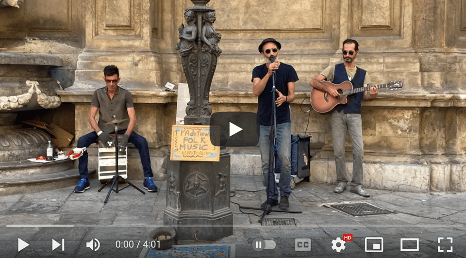 Image alt text: A still from a video of three musicians playing on a city street