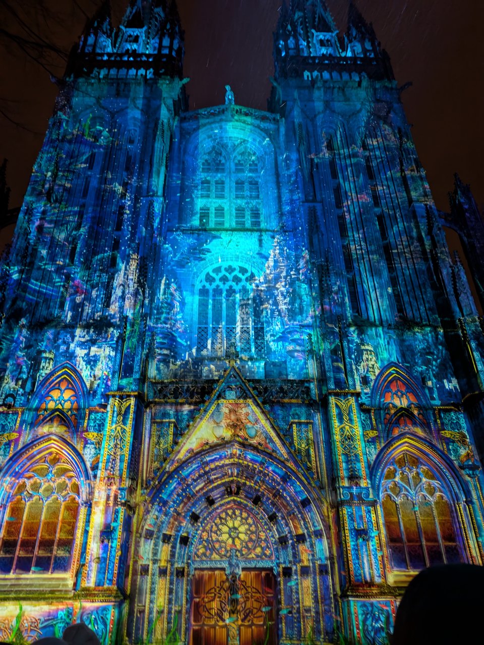 Photo of the Cathedral of Saint Corentin in Quimper, France, with bright multicolored lights projected onto its surface to highlight the gothic architecture.