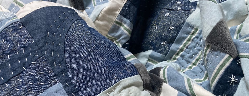 An improvisational quilt in shades of blue with white stitching.