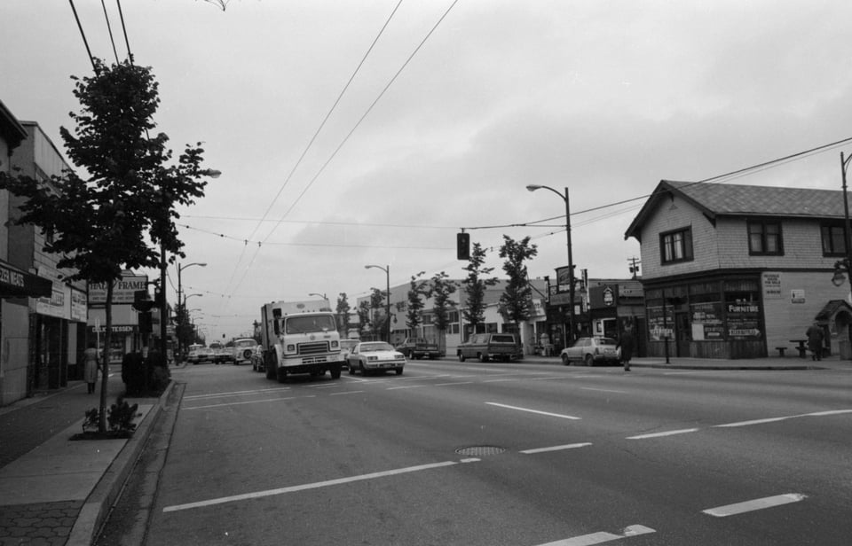 Black and white street scene showing businesses and well-manicured sidewalks planted with trees.