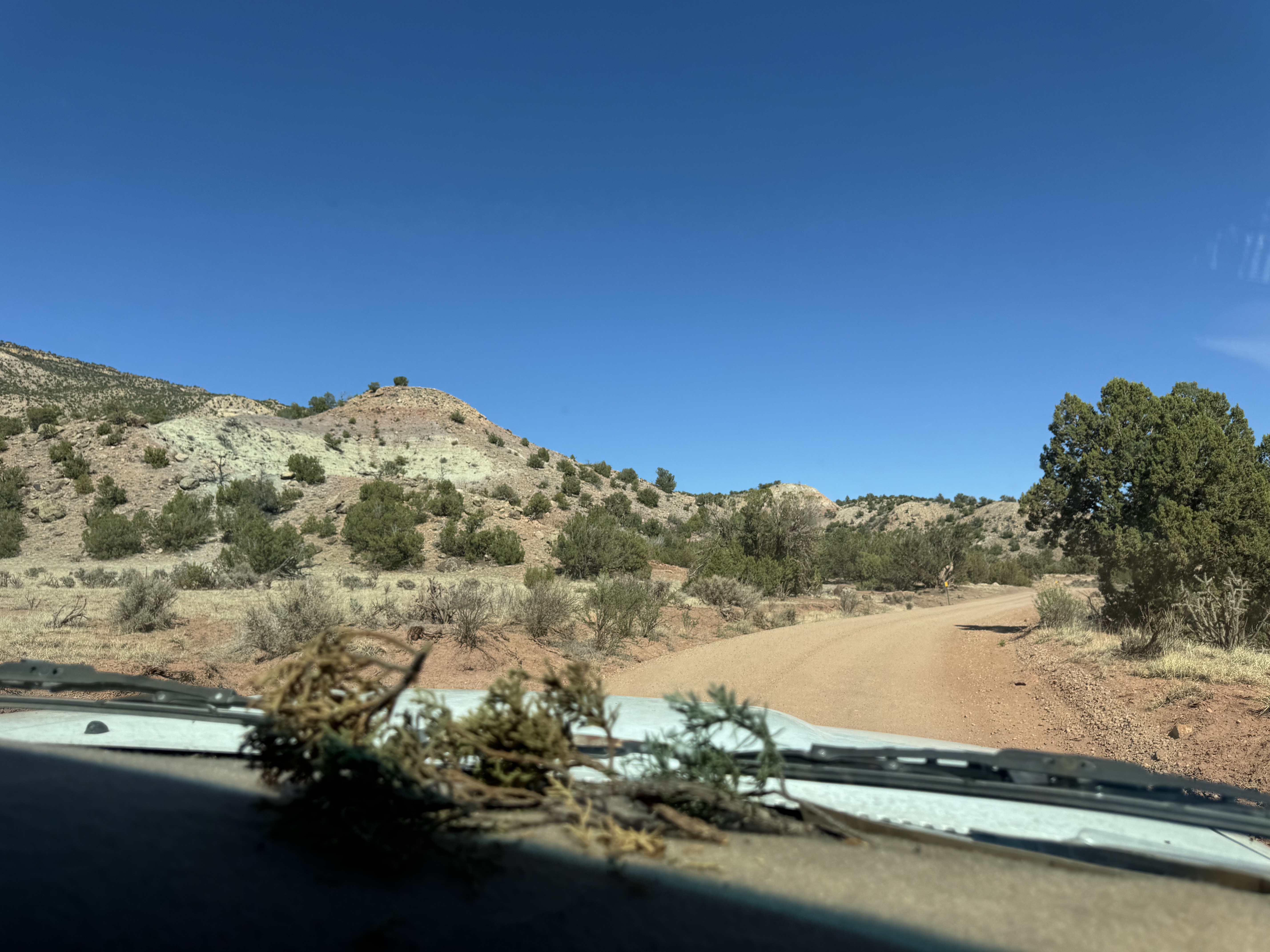 a blue sky with desert hills and a dirt road from looking out the windshield of  an old truck.