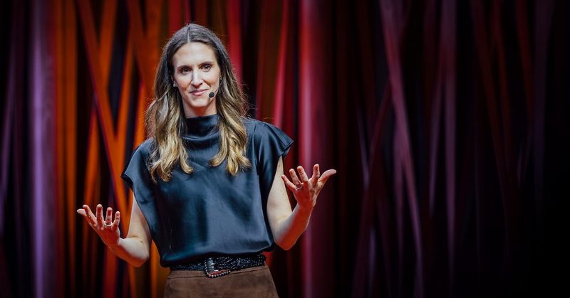 Sandra Matz on the TED stage, hands raised, in front of a red curtain