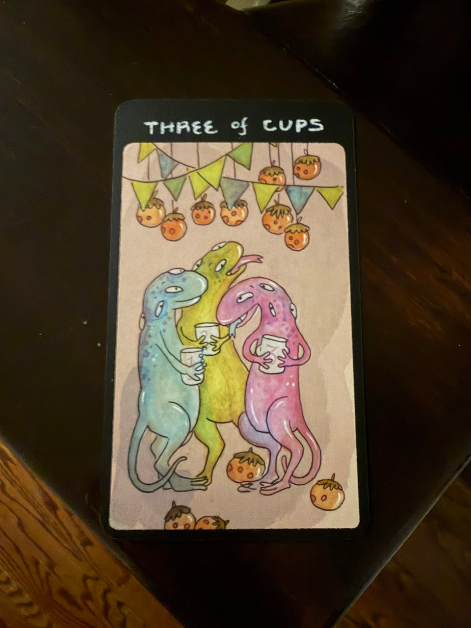 A card from Shing Yin Khor's Strange Beast Tarot Deck, Three of Cups, with three lizards standing around at a party, drinking together.