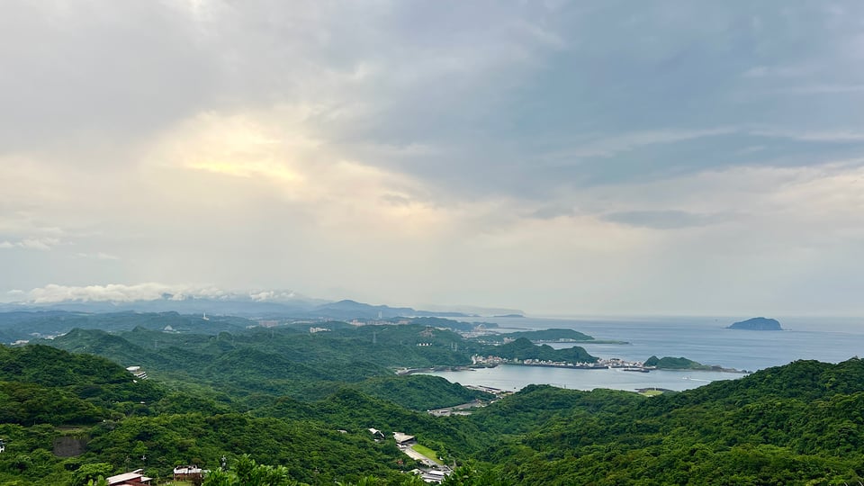 Panoramic image of verdant hills leading down to a seaside community, islands off shore