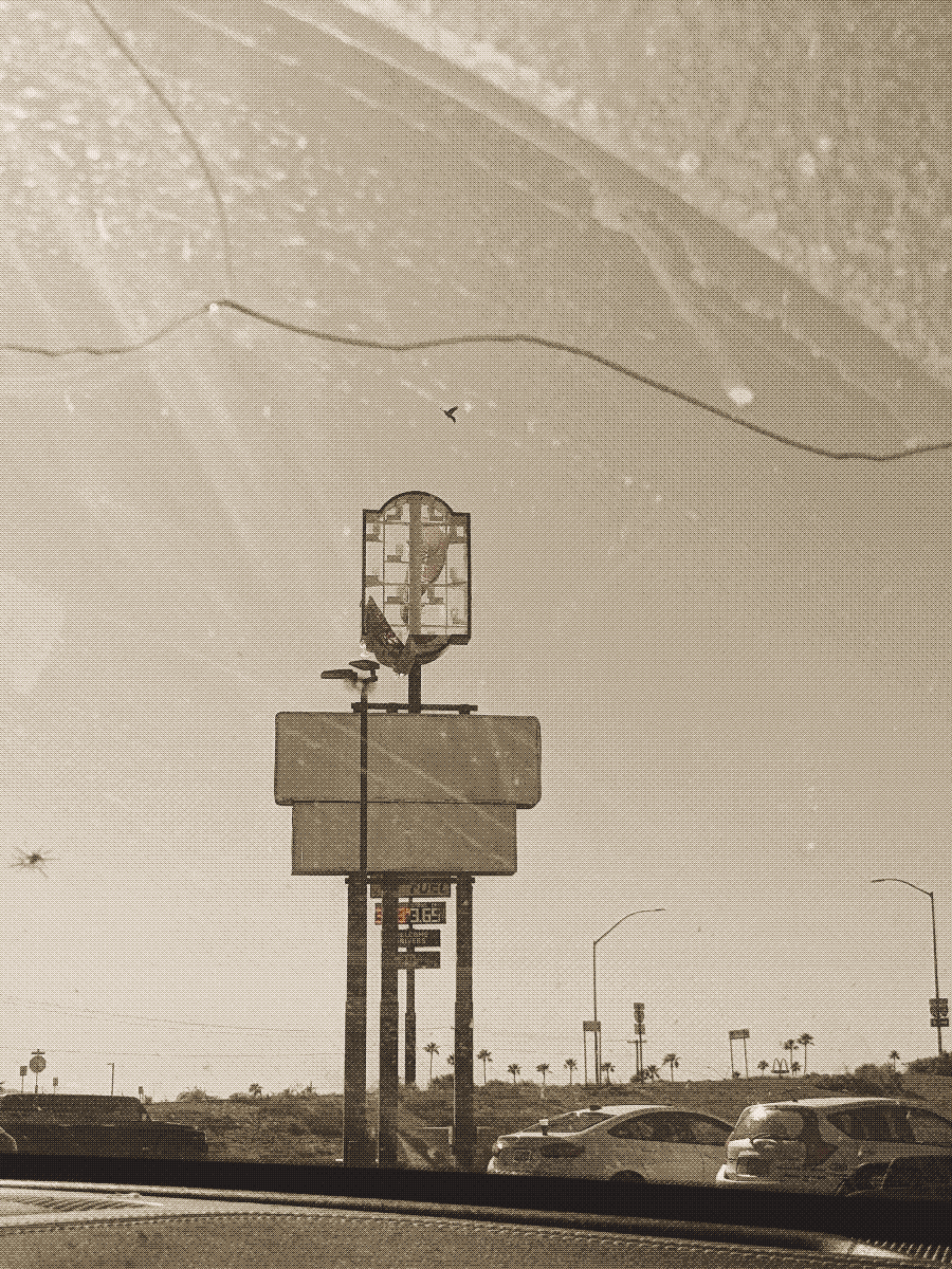 Sepia photo of a dilapidated motel sign photographed through a cracked windshield.