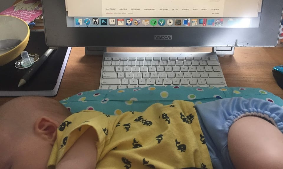 A photo of my desk from 2018 with a keyboard, mouse, sleeping baby and pacifier.