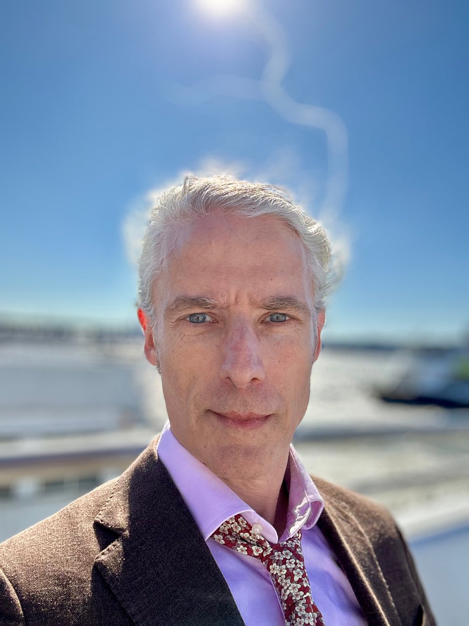 portrait-mode selfie of white man on ferry crossing Hudson. The sun is above his head, and while his hair is tied back, a strand or two are caught in the wind and flying above, illuminated. Also, he's got this combo of a brown sportcoat, pink dress shirt and red tie with yellow/white flowers, and with the collar unbuttoned, the whole combo REALLY works. At least, that's what the guy at the front desk of the hotel said.