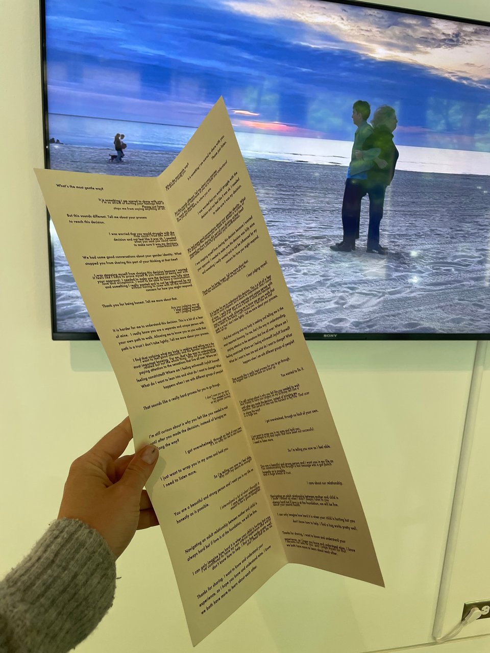 a hand holding a script infront of a video of two people back to back