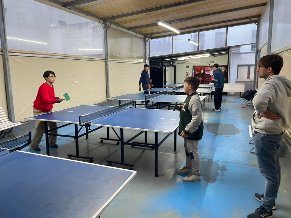 A woman and a boy play ping pong while a man looks on.