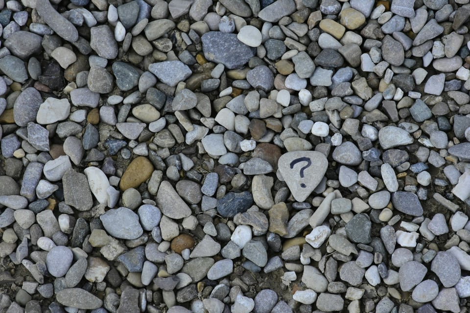 An overhead photo of stones. One stone has a question mark painted on it. Photo by Ana Municio on Unsplash.