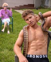 a shirtless man sitting on a lawn chair with a snake around him; an image of a woman in a wig and smoking has been copied and pasted into the background