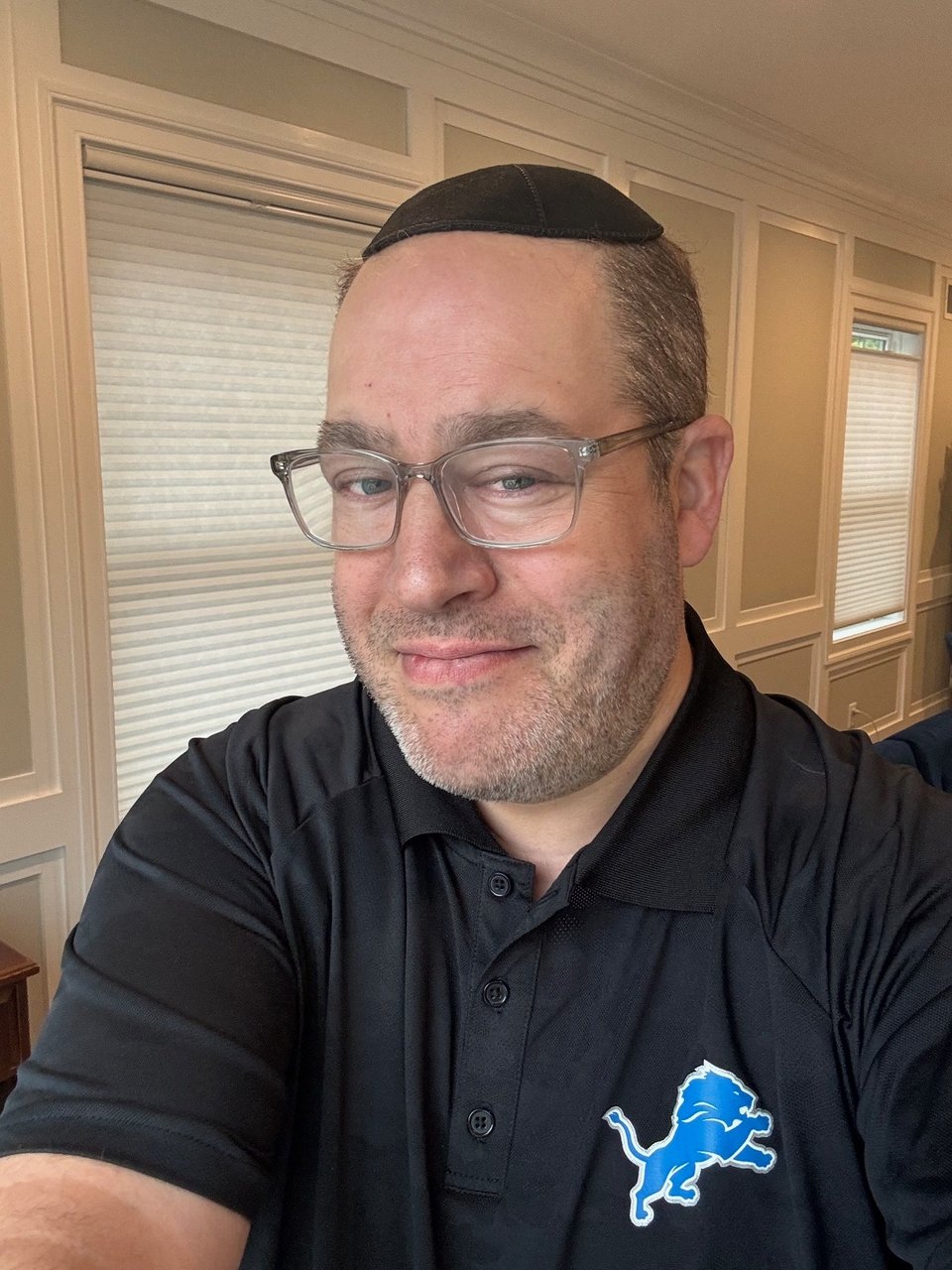 a picture of neil in a black polo shirt with a blue and white detroit lions logo on the left breast