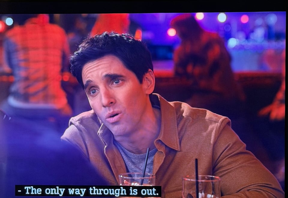 A screenshot of Paul W. Downs as Jimmy on the tv show Hacks. He is drunk and the caption reads "The only way through is out."