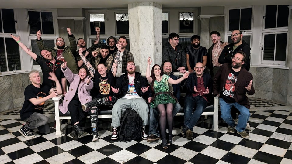 A large group of comics people cheering while sat on the bench in the toilets of the Majestic Hotel