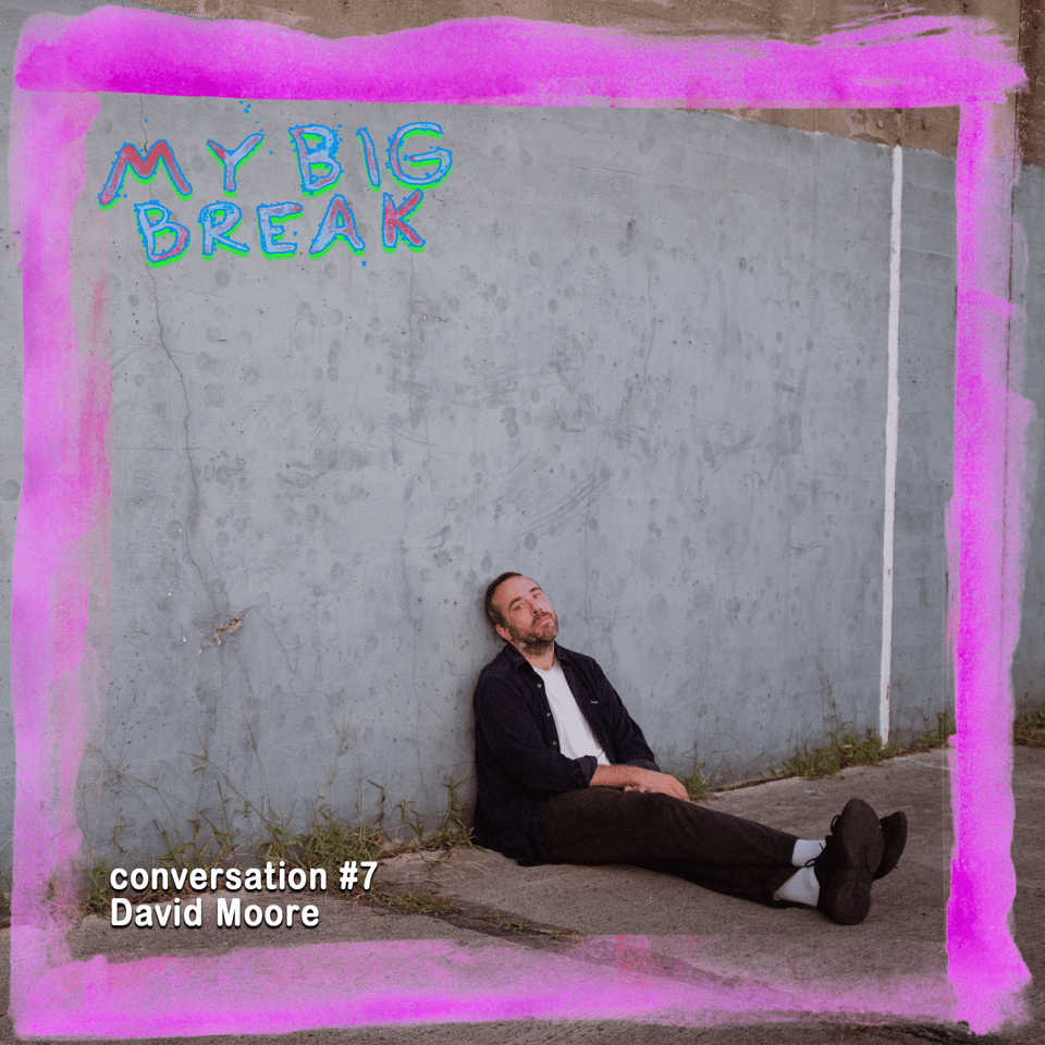 David Moore sitting languidly on a concrete sidewalk leaned against a building