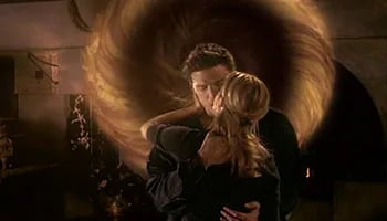 Buffy, with her back to the camera, embraces her boyfriend Angel, while a portal opens behind him