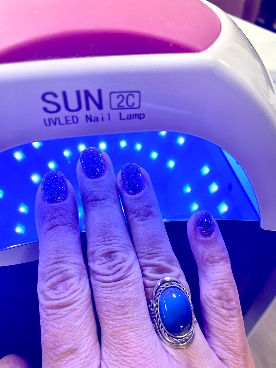A hand with the nails inside a UVLED Nail Lamp. The gel nails are purple glitter.