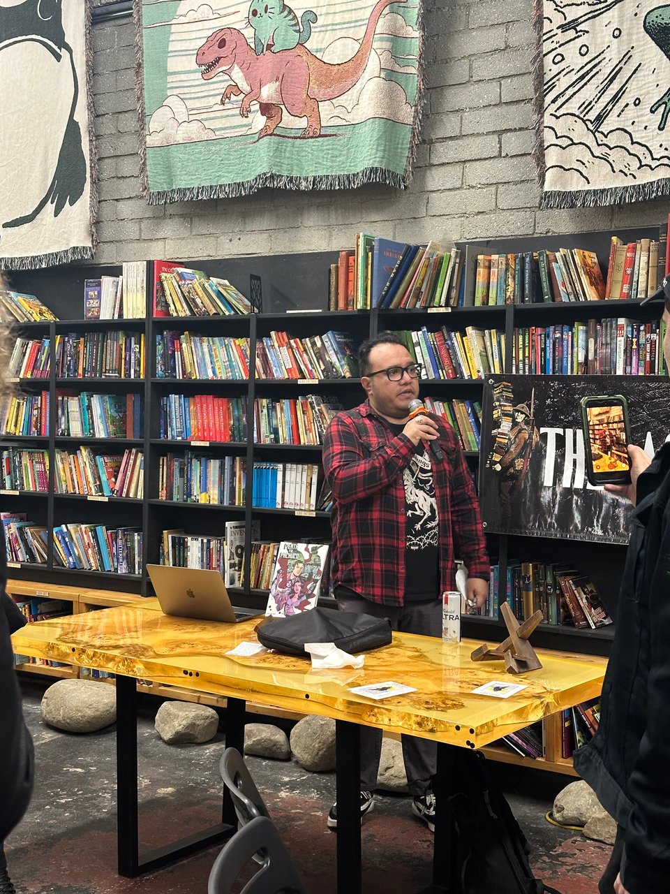 henry barajas at the last book store studio city. nice table. rock holding up bookshelf packed with books. nice rugs hung from the wall.