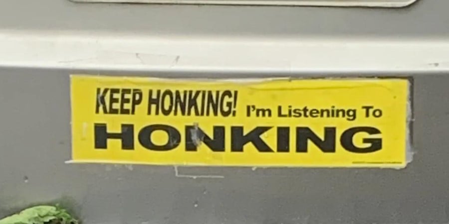 A photo of a bumper sticker that reads: KEEP HONKING! I'm Listening To HONKING