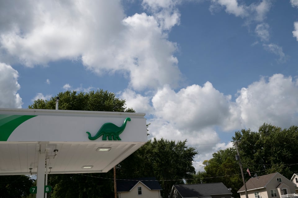 Photo of the awning of a Sinclair gas station, lookink up at a sky with big puffy clouds.