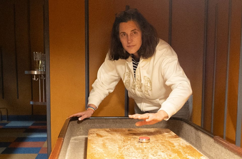 A woman in a white sweatshirt sends off the shuffleboard puck.