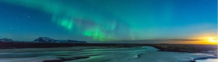 An aurora over a snowy landscape with a sun rising in the distance