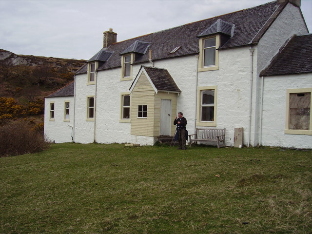 a white washed stone cottage with a man outside and hills in the background